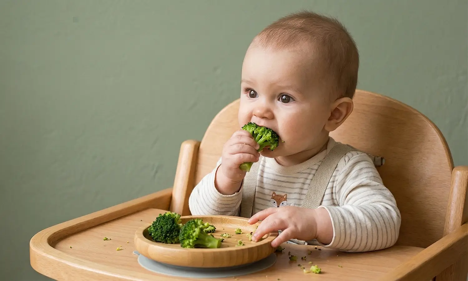 Baby reaching for a broccoli floret during their first weaning session